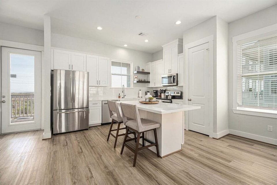 Gourmet kitchen featuring stainless steel refrigerator, spacious island, and open dining flow—perfect for large group stays in Galveston.