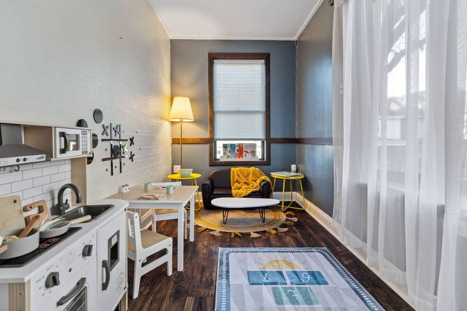 Bright, Playful, and Just Their Size – This inviting corner features a child-sized leather loveseat, vibrant yellow accents, and sheer curtains that catch the sunlight just right.
