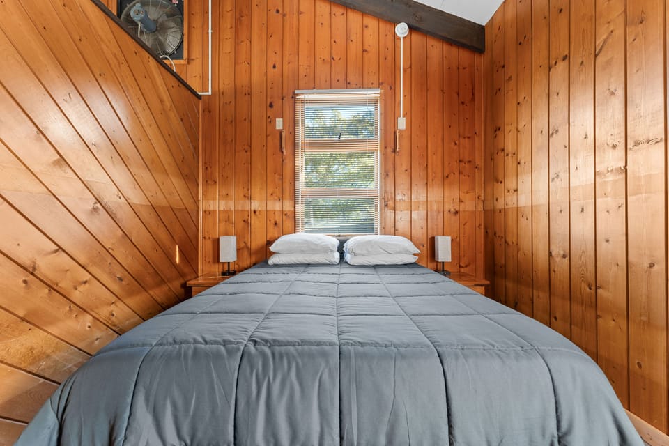 Cozy queen bedroom with rustic wooden walls, a peaceful setting for a great night’s sleep.