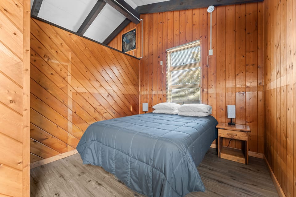 Cozy bedroom with rustic wood paneling and a comfortable queen bed—perfect for a restful night after a day of exploring.