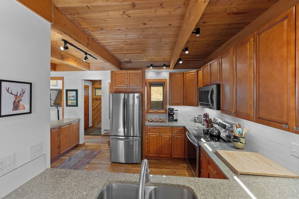 Your fully-equipped kitchen invites effortless meal prep with rich wood cabinetry, stainless steel appliances, and granite countertops—all beneath soaring timber-beamed ceilings that add warmth and rustic charm to your mountain retreat.