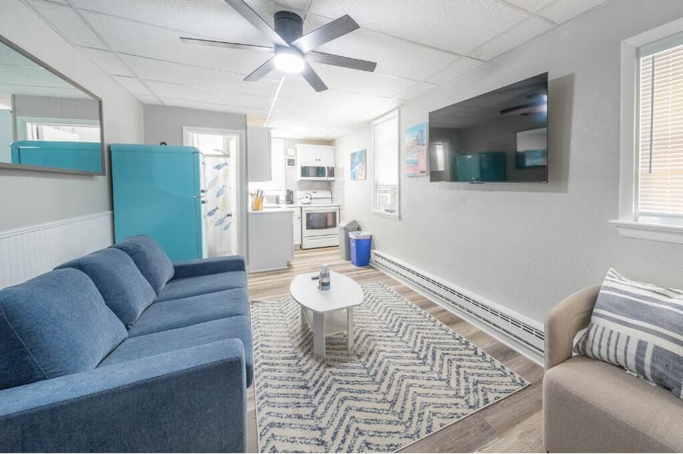 Relax in this cozy living area featuring a plush sofa, flat-screen TV, and cheerful beach vibes. The vibrant retro fridge adds charm to the fully equipped kitchen just steps away.