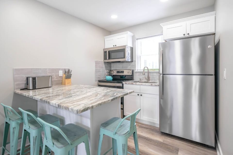 Bright, modern kitchen with stainless steel appliances, granite counters, and charming aqua bar stools – perfect for cooking and casual dining.