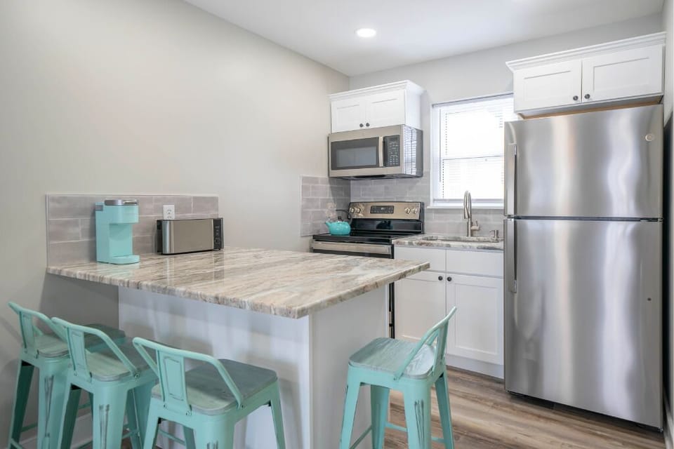 Bright modern kitchen with stainless steel appliances, spacious island, and bar seating. Fully equipped for cooking and dining, with clean finishes and coastal touches for a fresh, inviting feel.