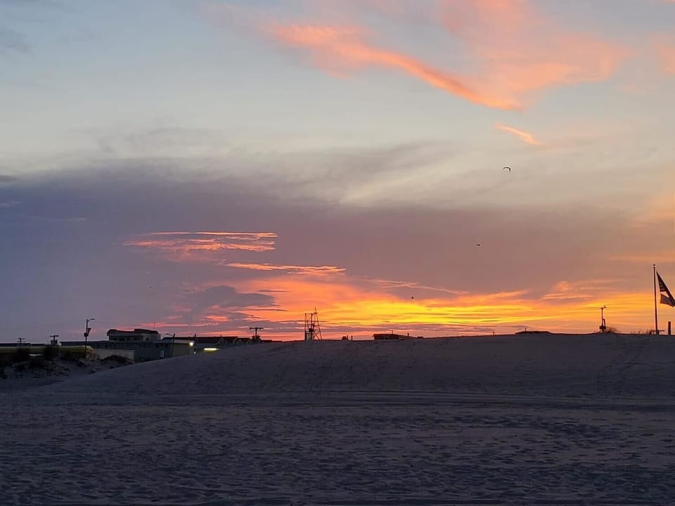 Golden hues stretch across the sky as the sun sets behind the dunes, painting the evening with warmth and calm. A peaceful moment to end a day by the sea.
