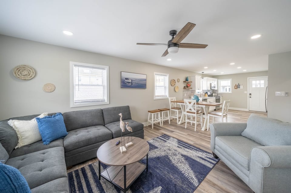 Open-concept layout with a coastal-chic vibe, featuring a comfy sectional, full dining set, and a bright, fully equipped kitchen. Ideal for relaxing, dining, and spending quality time together.