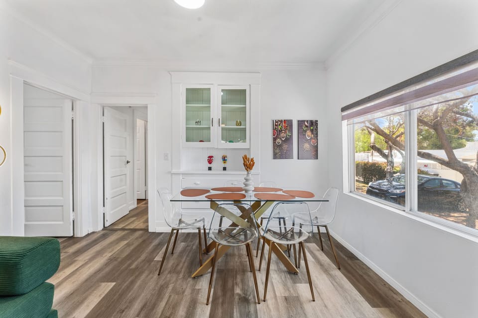 Elegant dining with glass table, acrylic chairs, warm tones, and modern flair.
