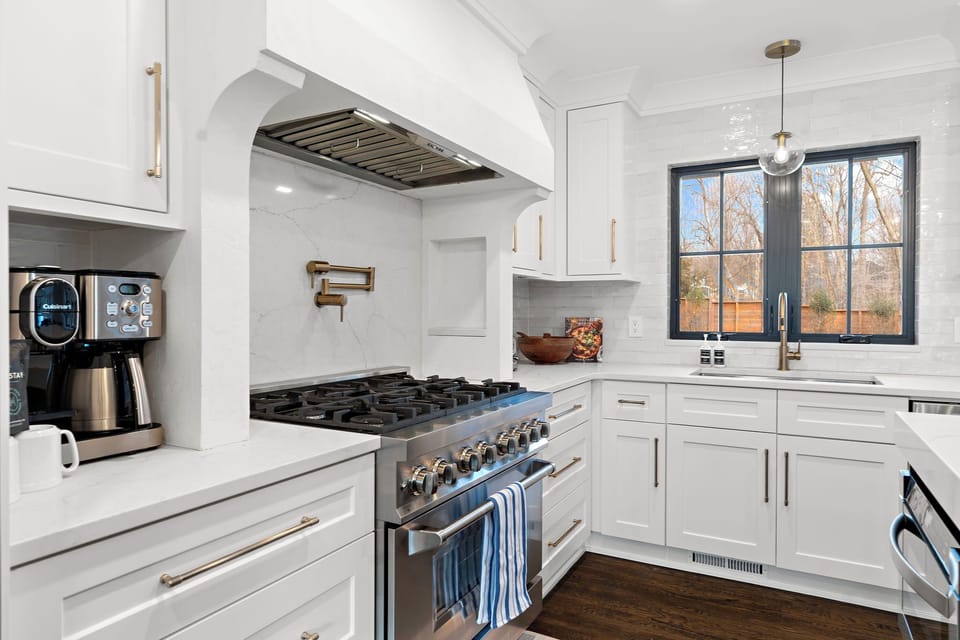 Your gourmet kitchen awaits with professional-grade gas range, marble countertops, and gleaming white cabinetry bathed in natural light.