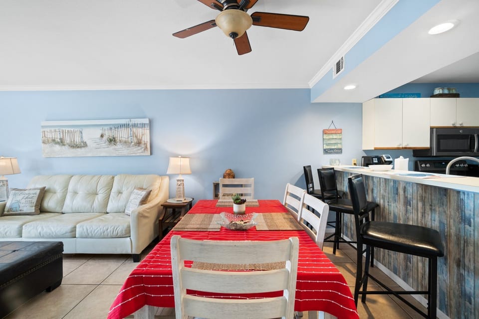Dining area with a red-striped tablecloth and open kitchen with bar seating in a cozy, modern space.