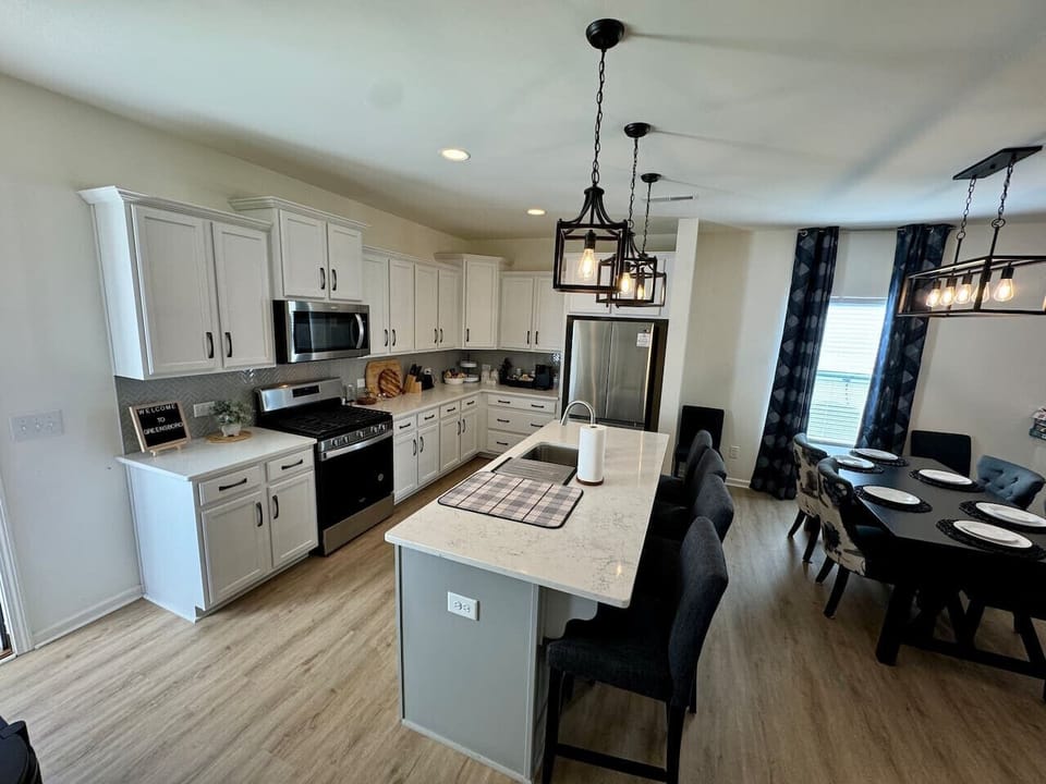 Modern kitchen with white cabinets, island, pendant lights, barstools, and adjacent dining area.