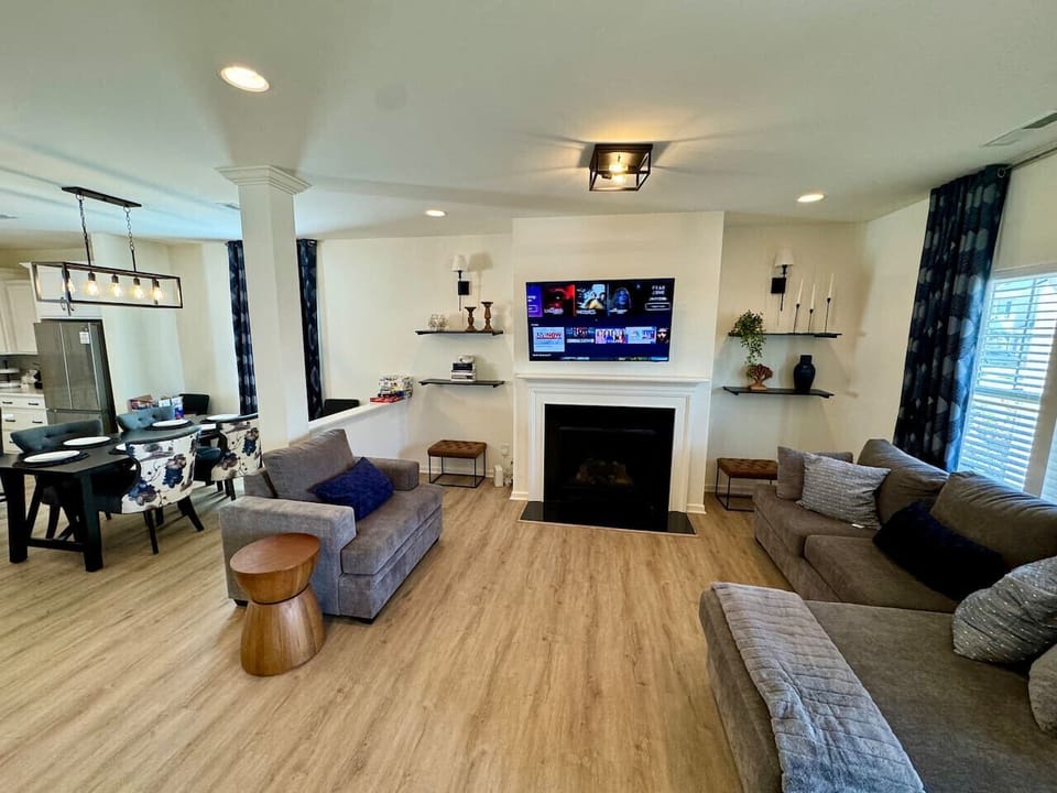Modern living area with gray sofas, fireplace, mounted TV, floating shelves, and dining space.