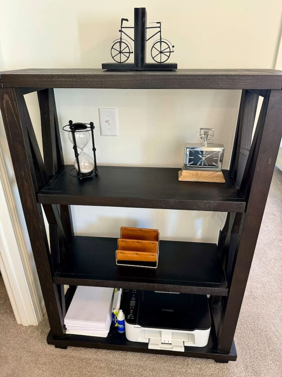 Dark wooden bookshelf with decorative items, an hourglass, a clock, a file organizer, and paper storage.