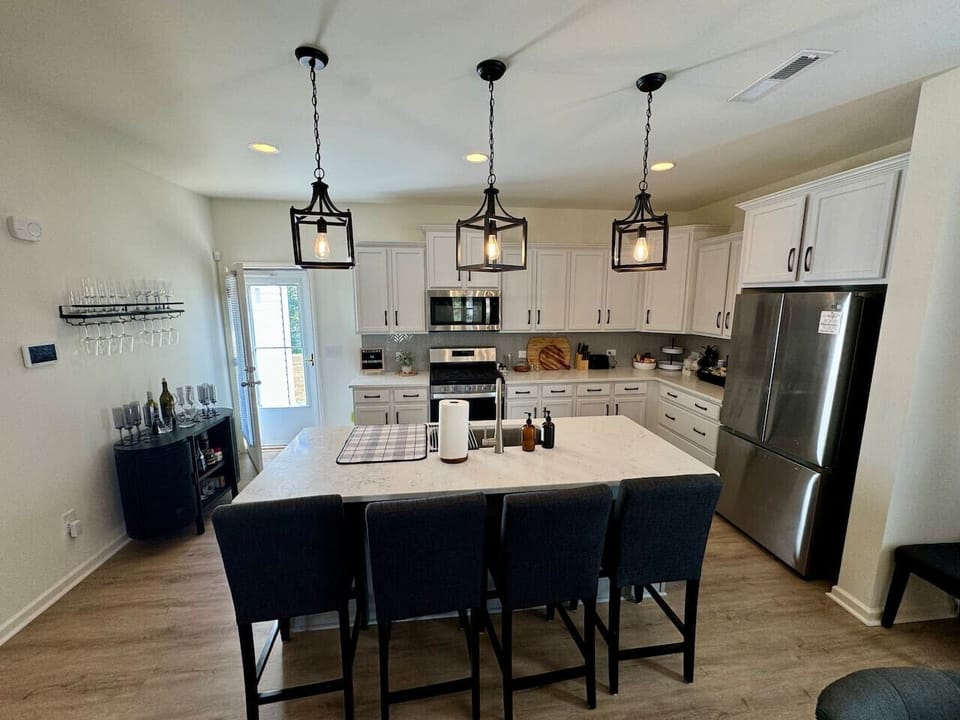 Modern kitchen with white cabinetry, pendant lighting, island, barstools, and glass rack.