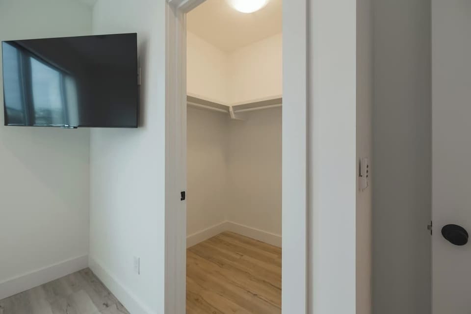 Walk-in closet with wooden flooring, next to a wall-mounted TV.