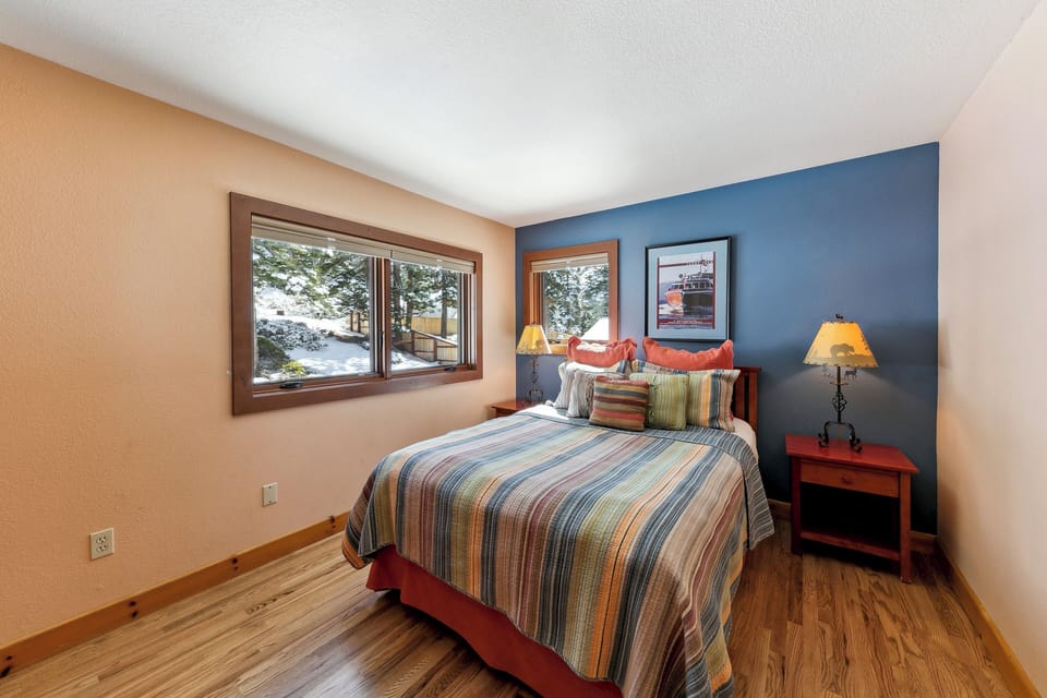 Wake up to snowy mountain views from your cozy bedroom with warm wood accents and vibrant striped bedding.
