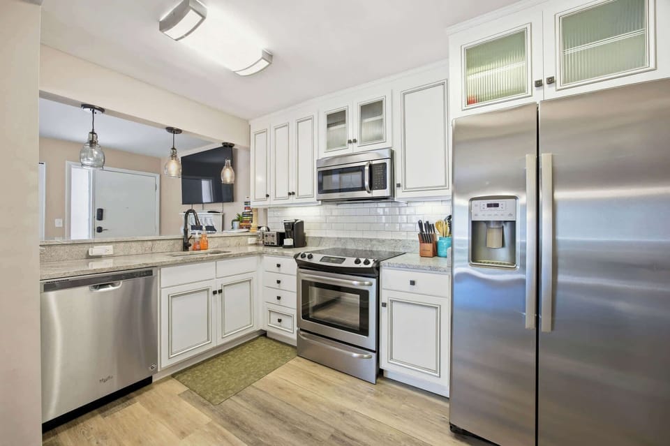 White cabinetry and glass-front doors bring a sense of airy openness to this modern chef's corner. Speckled counters and brushed metal appliances create a sleek yet warm space for preparing morning coffee or a quiet dinner at home.