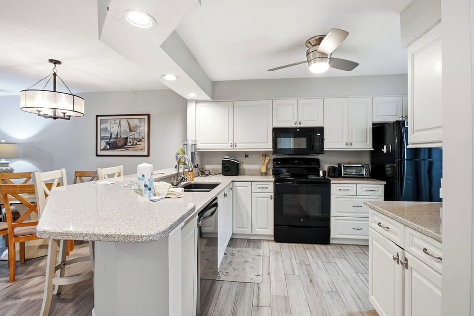 Polished stone counters and crisp white cabinetry create a bright, airy hub for morning coffee. This modern kitchen flows seamlessly into the dining area, illuminated by soft overhead glows and clean design details.