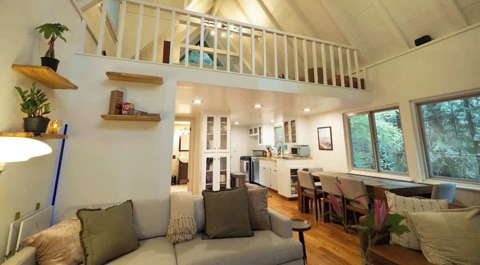 This airy open-concept space features soaring ceilings, a charming loft above, cozy seating, and a bright kitchen and dining area, creating a warm and inviting place to gather and relax