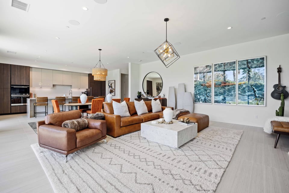 Spacious living area with leather sofas and elegant chandeliers overhead.