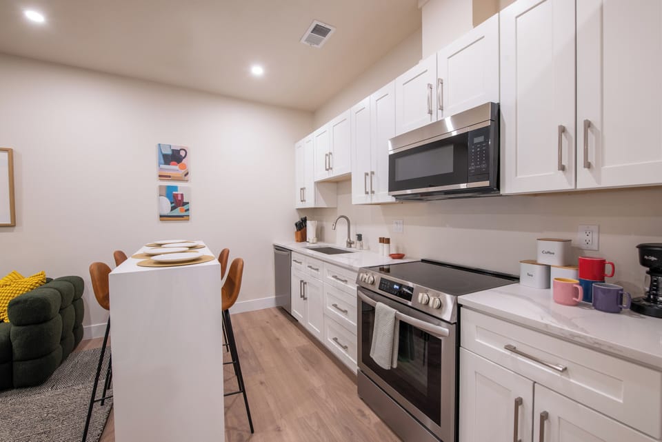 - Modern kitchen features a full size oven, microwave, dishwasher, and extra white cabinetry
- Sleek quartz countertops and minimal decor make the space feel bright and functional
- Four bar stools line the counter for easy dining or morning coffee