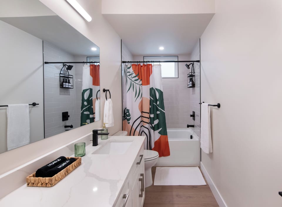 - Stylish bathroom features a bold curtain, wide vanity, and oversized mirror with modern lighting
- Tub and shower combo includes matte black fixtures and built in caddy
- Soft wood look floors and white cabinetry bring a clean fresh finish