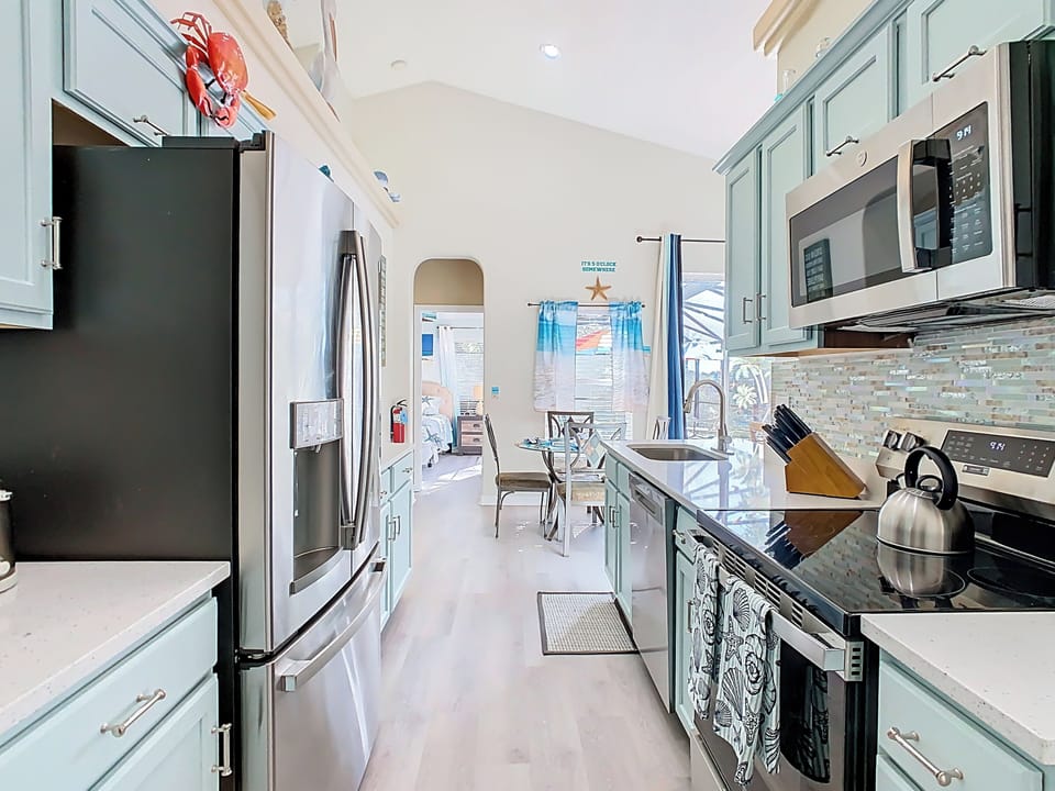 - Coastal kitchen with ocean toned cabinets & a scenic peek into the sunny bedroom
- Sleek stainless appliances, double sink, & full cookware setup make mealtime a breeze
- Bright & open with beachy flair, perfect for casual mornings or big family dinners