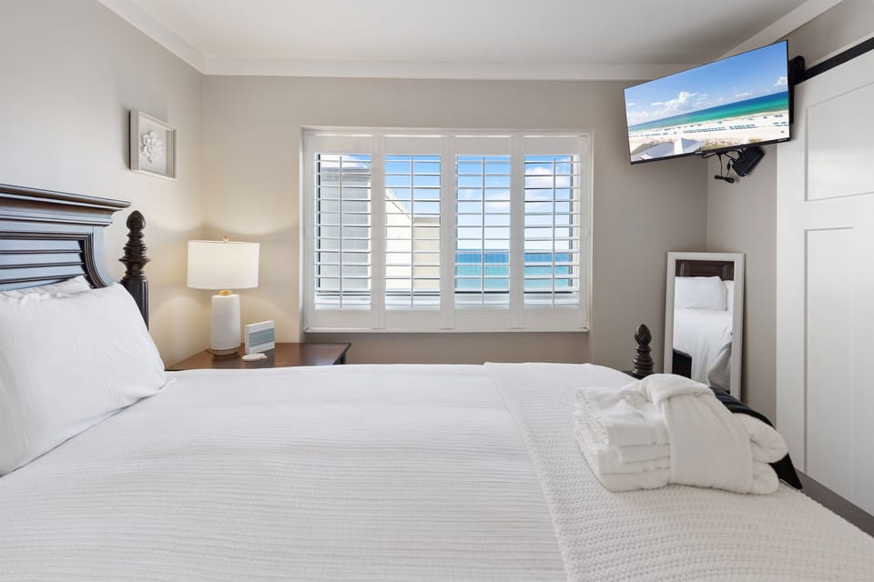 Wake up to turquoise waters through your plantation shutters in this serene bedroom, where crisp linens and ocean breezes promise perfect mornings.