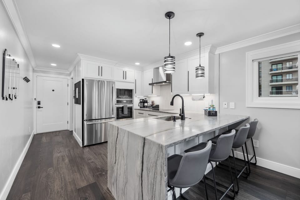 Sleek chef’s kitchen with waterfall island, bar seating & SS appliances.
