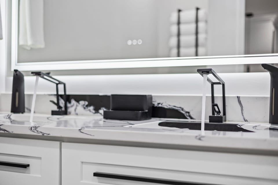 Designer double vanity with backlit mirror and matte black fixtures.