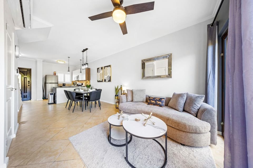 Open-plan living space with with a ceiling fan, with a modern kitchen and comfortable seating area.