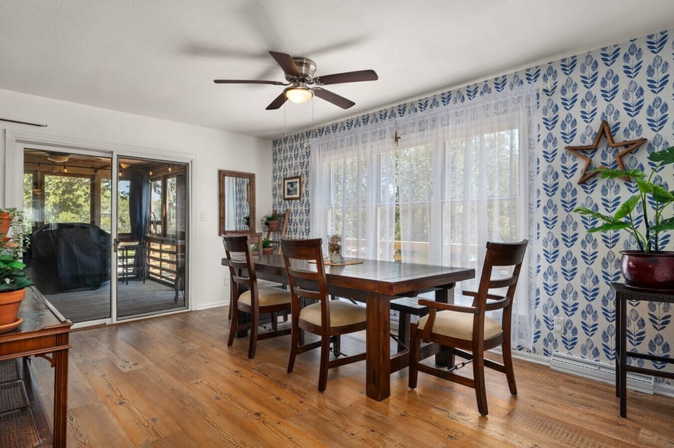 Sunlit dining area w/ wood table & chairs, set beside large windows for easy meals & gatherings.