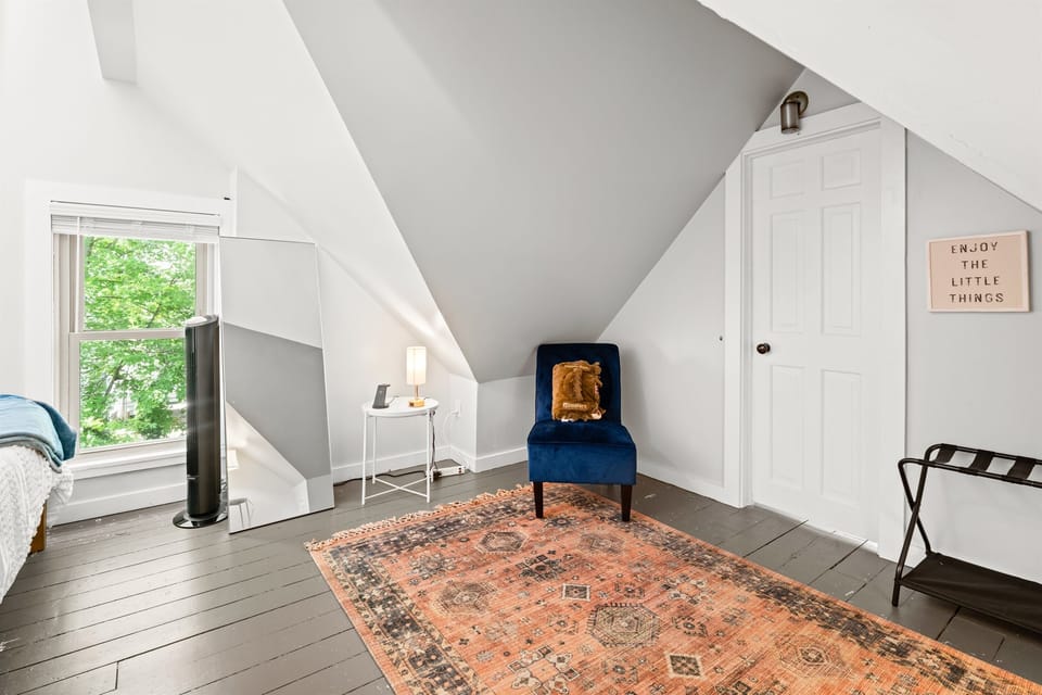 Bedroom 2 (upstairs) has a sitting chair, mirror, charging cables, and tons of natural light.