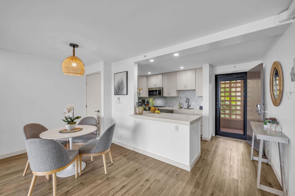 Features a modern round dining table with seating for four in grey upholstered chairs, highlighted by a warm woven pendant light.