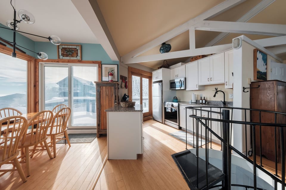 This bright, open space connects the kitchen, dining area, and spiral staircase leading to lower-level bedrooms. Ideal for group stays, cooking together, and soaking in the views.