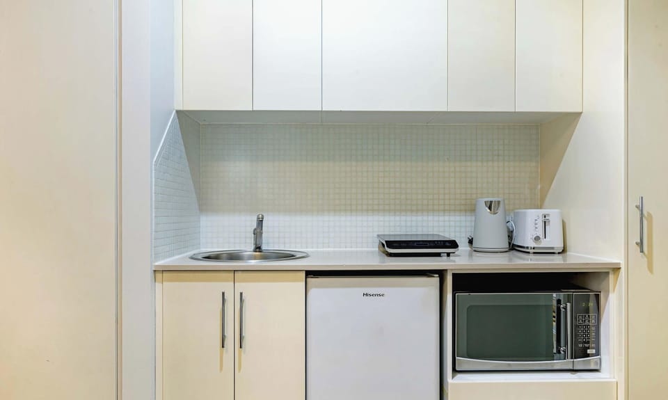Compact kitchenette with sink, microwave, bar fridge, cabinetry, and tea/coffee facilities.