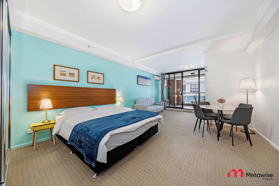 Spacious bedroom featuring a comfortable king-size bed, bedside tables with lamps, teal feature wall, and balcony access.