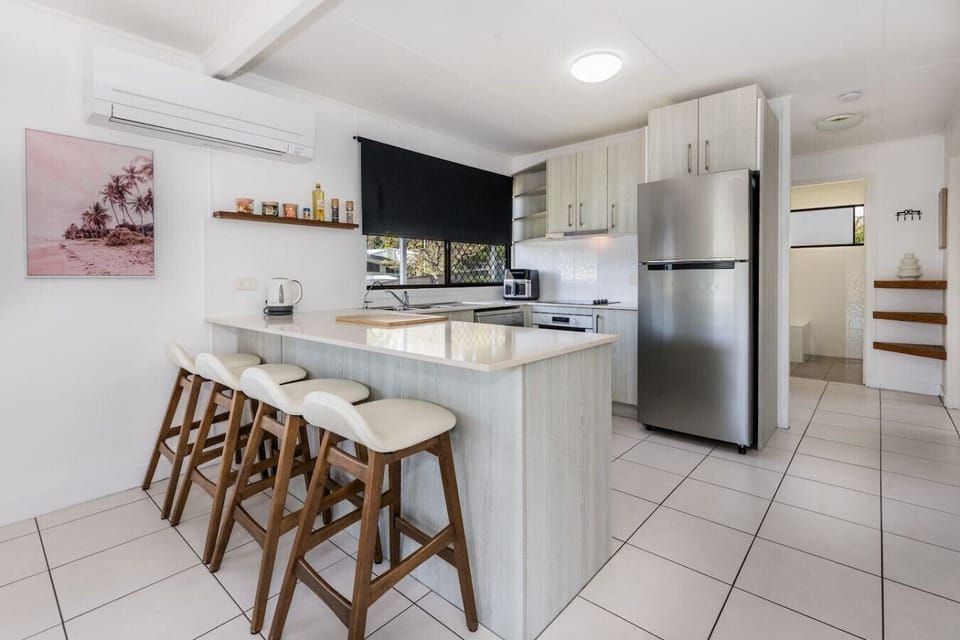 Kitchen with island bench, timber stools, stainless appliances, and coastal décor. Family‑friendly, fully equipped cooking space.