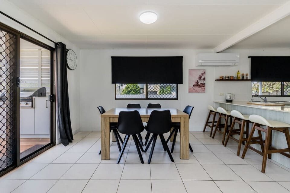 Dining + kitchen with timber table, black chairs, island bench, and coastal décor. Family‑friendly, fully equipped cooking and dining space.