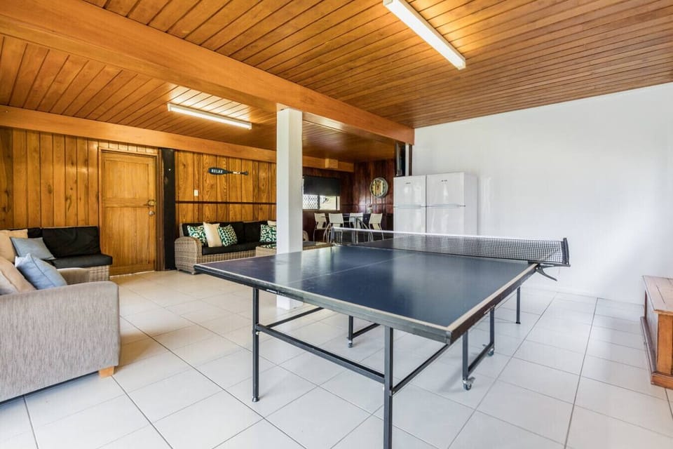 Indoor recreation room with ping pong table, wicker seating, timber walls, and leisure space. Family‑friendly area for games and gatherings.