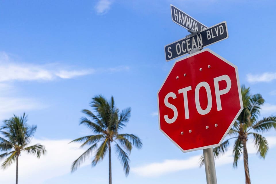 Stop sign at the intersection of hammon avenue and south ocean boulevard with palm trees under a clear blue sky