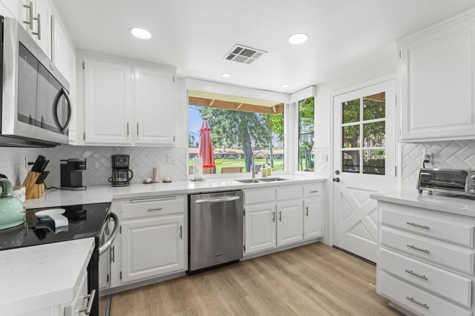 White kitchen w/ stainless appliances & windows framing peaceful outdoor views