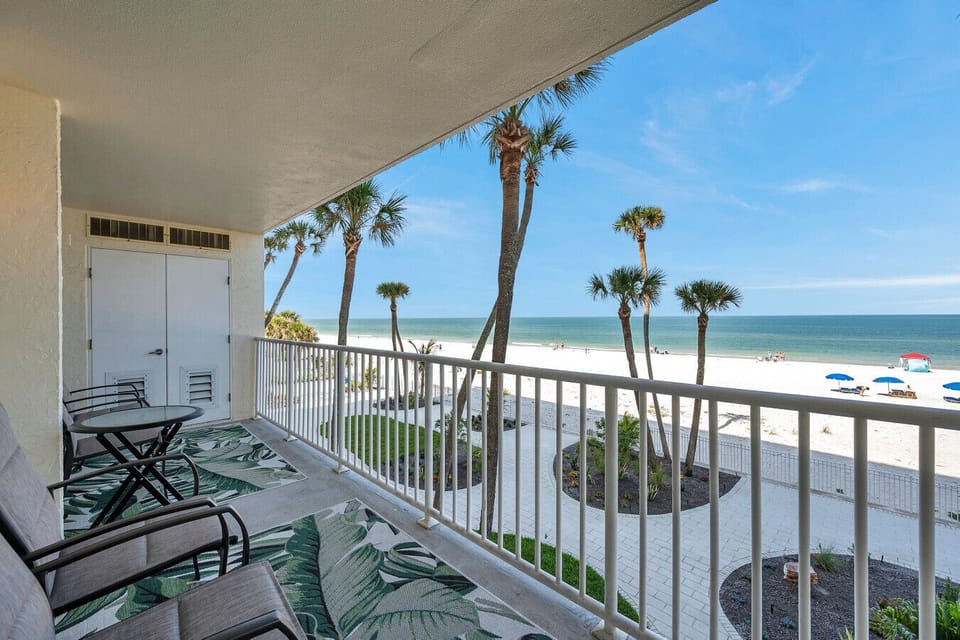 Breezy balcony w/ seating and palm-lined views overlooking the beach.
