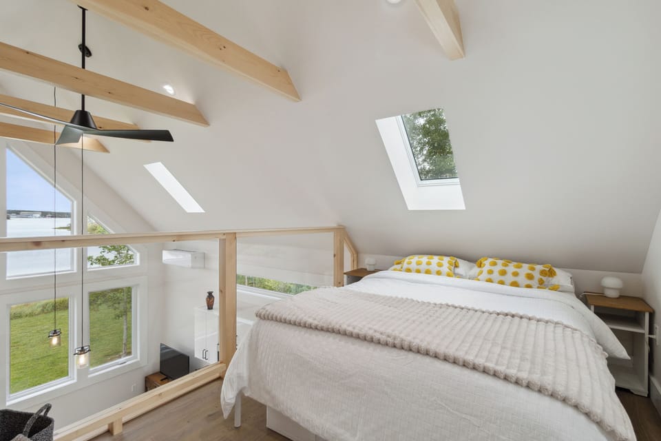 Cozy loft bedroom with skylights, wood beams, and breathtaking waterfront views.