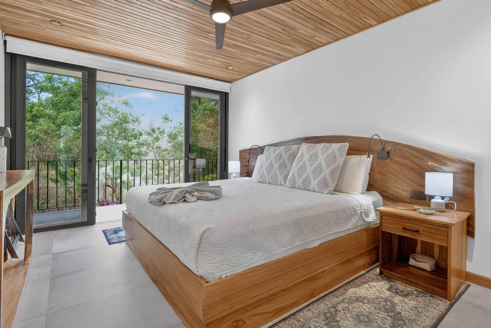 Natural wood accents shape the bed frame, headboard, and nightstand beneath a ceiling of wooden planks and a modern fan.