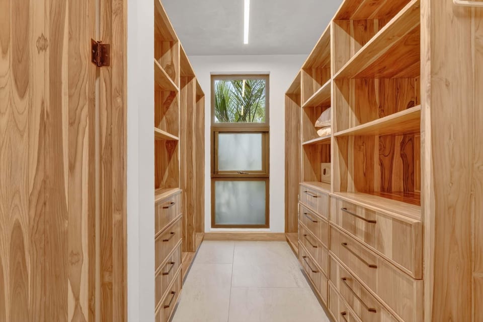 Walk-in closet with light wood shelves, multiple drawers, frosted glass window, and natural light from upper window.