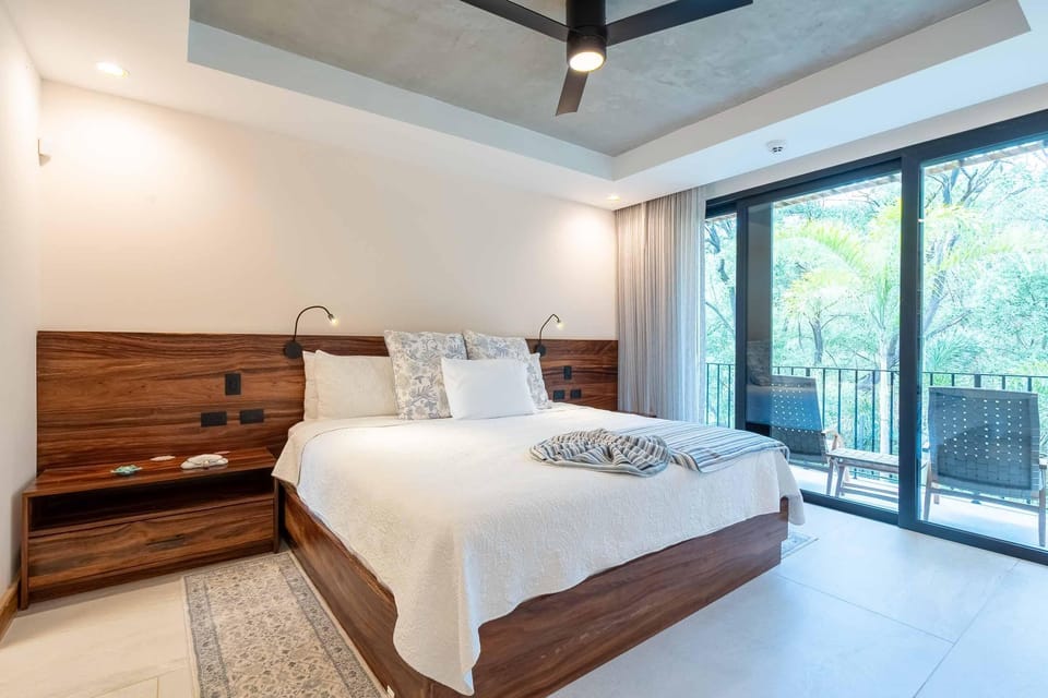 King bed with white quilt and floral pillows sits against a walnut headboard beside sliding glass doors.