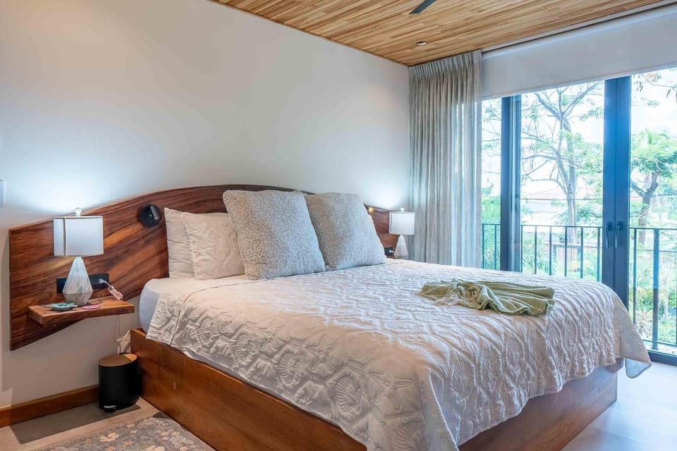 King bed with carved wood headboard flanked by floating nightstands and glass doors opening to a balcony.
