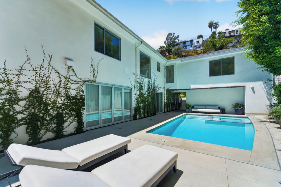 A sleek courtyard pool leads to an integrated spa and shaded lounge, framed by climbing greenery and potted plants.