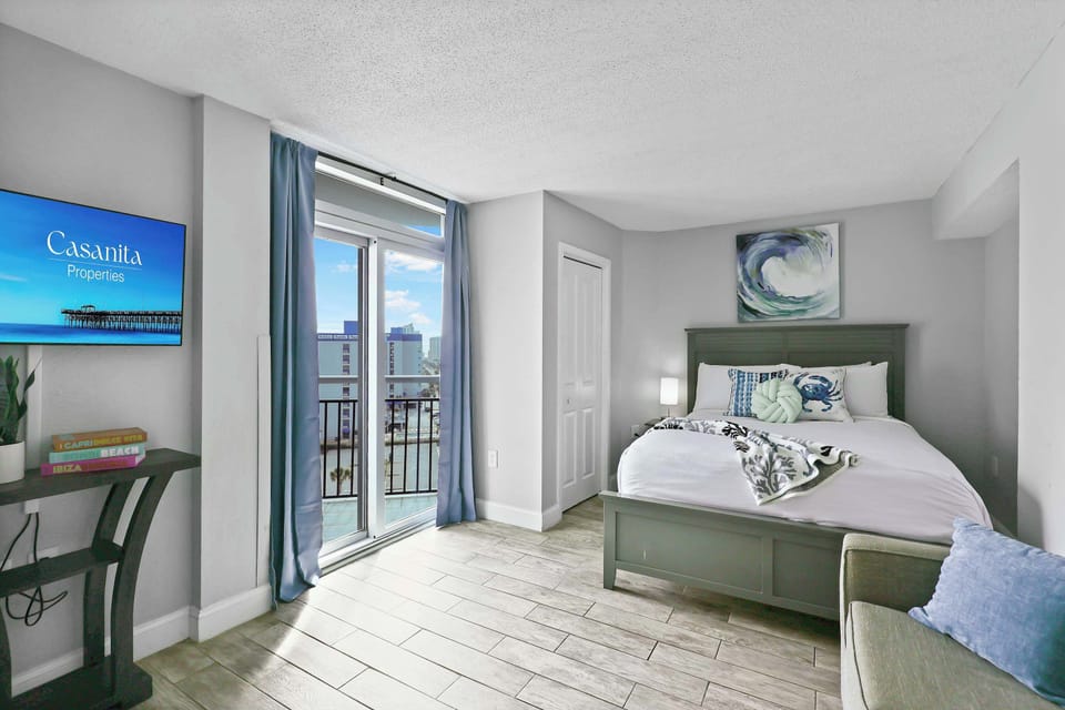 Relax in this serene coastal bedroom featuring a comfy bed, stylish decor, smart TV, and private balcony access. The perfect blend of comfort and charm for your Myrtle Beach escape!