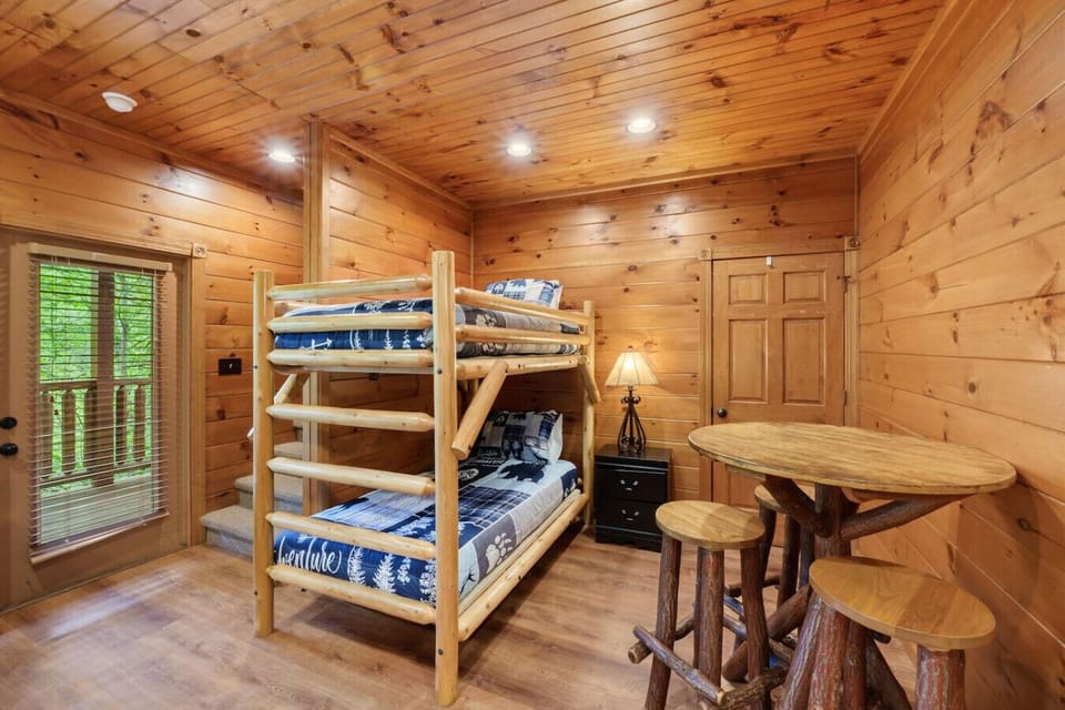 This inviting bunk room features a log-frame twin-over-twin bunk bed, rustic log table and stools, and easy access to the back porch.